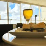 A glass of beer at the airport, alongside a sandwich on a plate