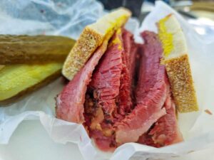 Large chunks of smoked meat inside two small pieces of bread. On the side you can see pickles.