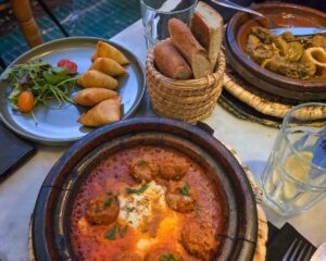 A small table with three dishes. A beef meatballs tagine, a plate with five cheese-filled filo triangles, and a lamb tagine.