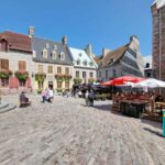 The main square in Quebec City, with typical stone buildings and cobbled stones on the ground. The windows of the houses have pink flowers in large pots underneath.
