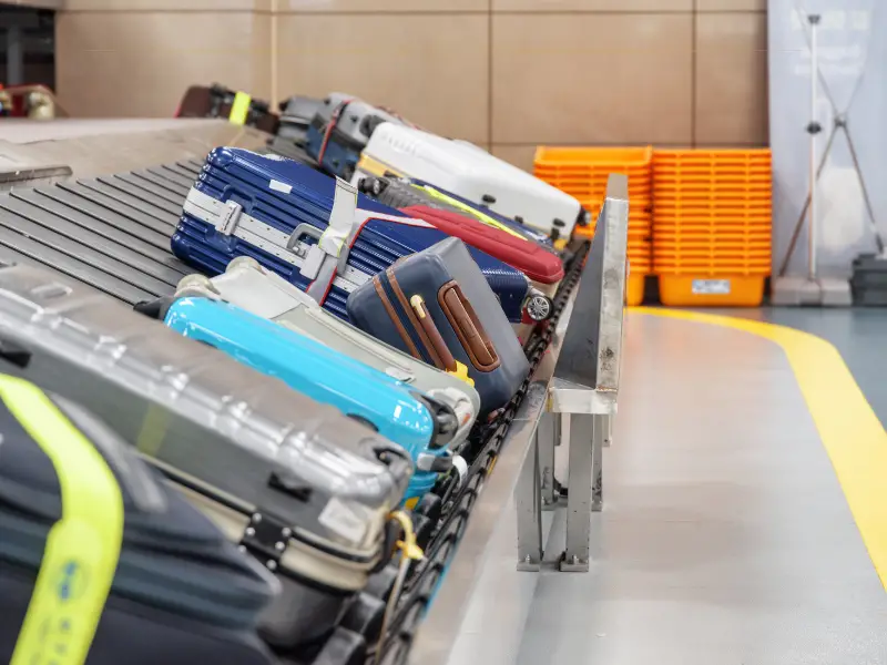 Different coloured bags on the carousel, in the arrivals hall of an airport.