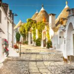 A cobbled street between trulli in Alberobello, which are decorated with red Christmas flowers.
