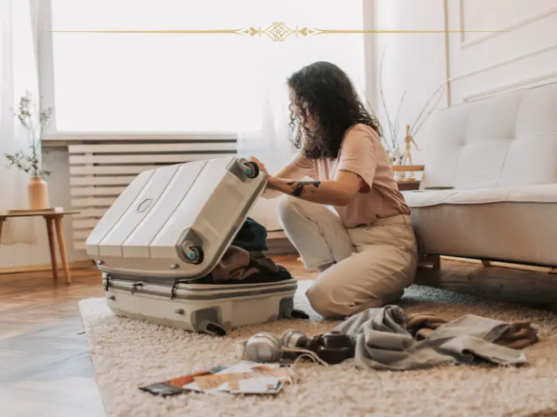 A woman packing a suitcase in her living room. There are electronic items on the floor next to her.