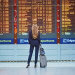 A woman wearing a suit and high heels, looking towards the departure board at the airport.