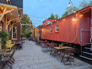 A red caboose in the train station, with tables and chairs in front and fairy lights going from it to the building.