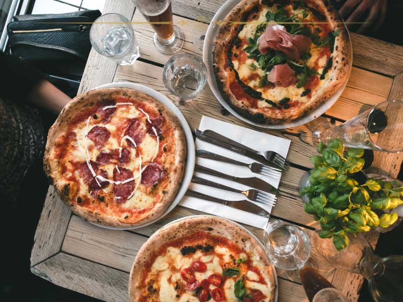A wooden table with three pizzas on it, photographed from above.