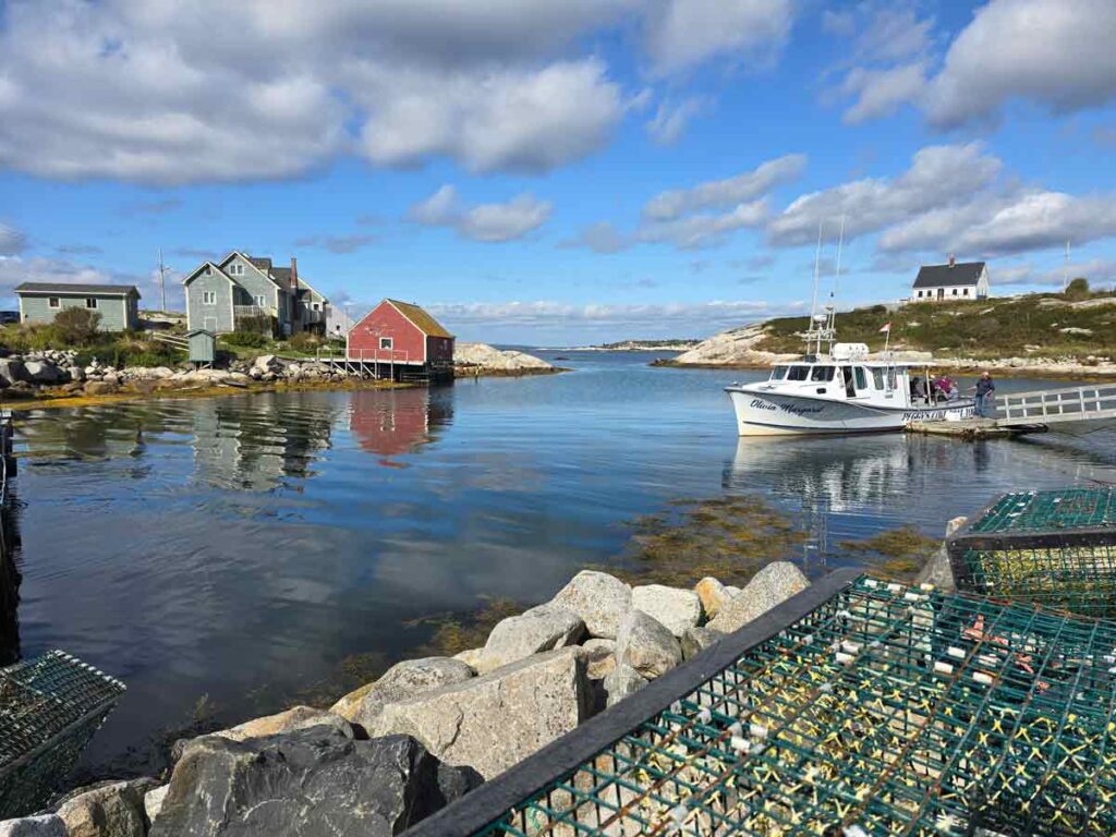 A serene scenery from Peggy's Cove, with a small bay with wooden houses on the shore, a lobster trap, and a white small boat.