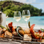 The Flavours of the Mediterranean You’ll Never Forgive Yourself for Skipping A seafood platter with two glasses of white wine in the background, against a sea background