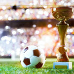 World Cup 2026 Dreams Face Reality Check as Trump's New Policies Threaten International Tourism A football next to the World Cup trophy, on a football field.