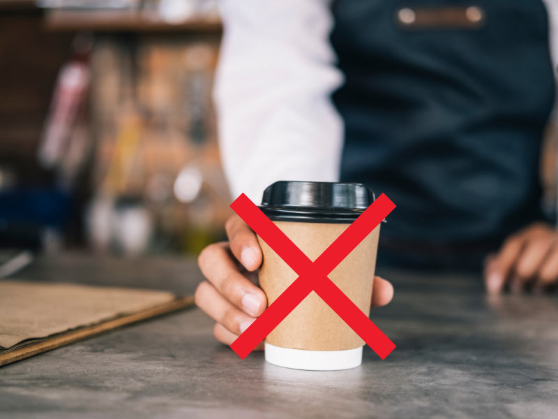 A close-up on a barista hand hanging in a coffee cup, with a red x on it.