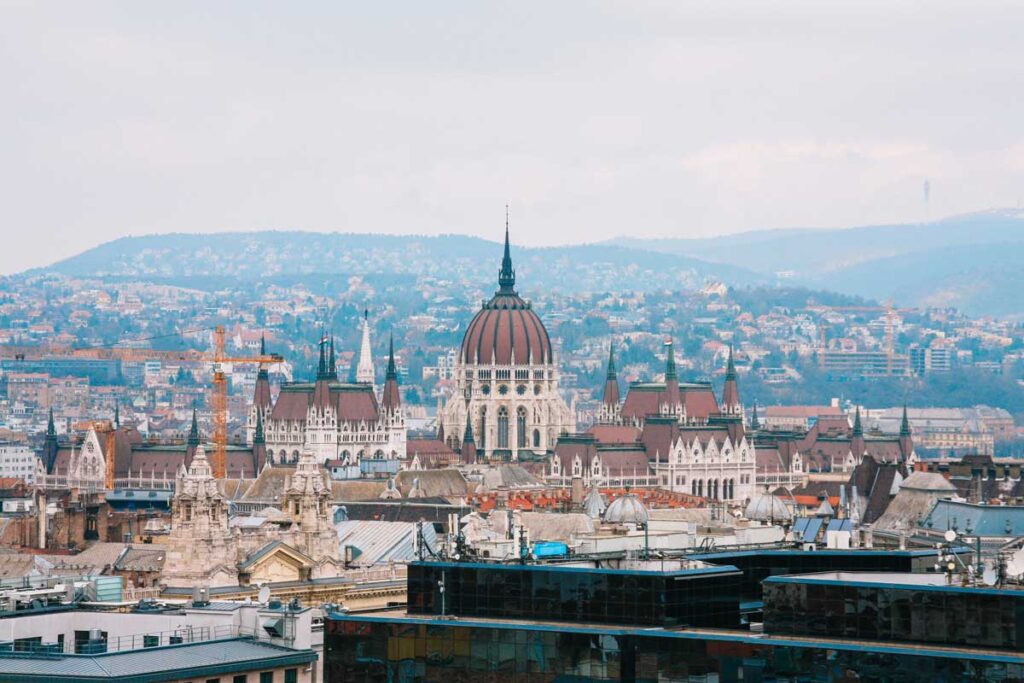 A photo of the Hungarian Parliament rising over the rooftops around it. Behind, you can see the Buda hill
