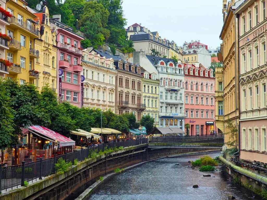 Pastel coloured buildings on the side of a river, in Karlovy Vary