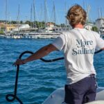 More Sailing Review – My First Sailing in Croatia Experience A man wearing a white tshirt with More Sailing written on it, holding rope, on a catamaran