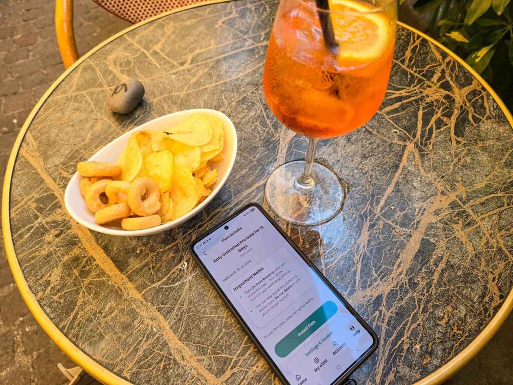 A table with an Aperol spritz, a bowl of crisps, and a phone with the esim app opened on it.