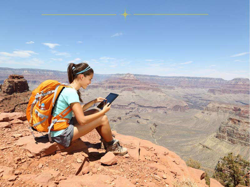 A woman on her phone, sitting down on the rim of the Grand Canyon.