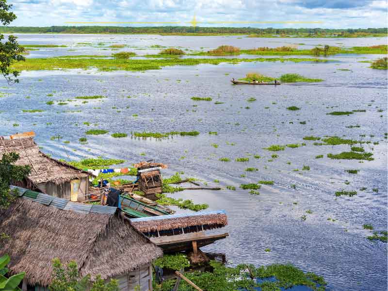 A slice of the Amazon river, with small wooden houses built on the shores, and greenery throughout the water